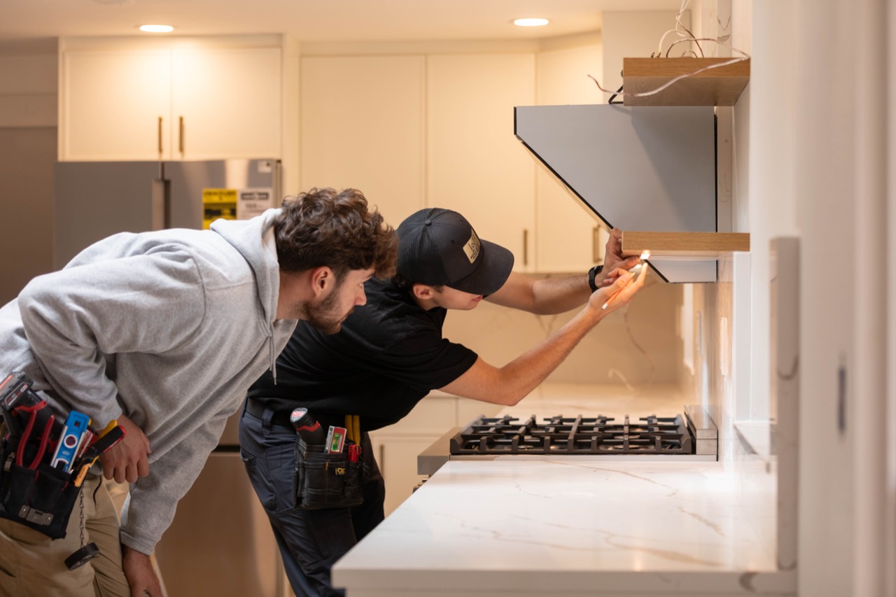 Electricians fitting lighting beneath a kitchen shelf